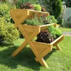 A wooden tiered planter filled with various herbs and lettuces sits on a green lawn in a garden setting. Produktbild-Vorschau