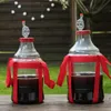 Two large glass carboys filled with dark liquid, each adorned with red ribbons, sit on a wooden table outdoors. Produktbild-Vorschau