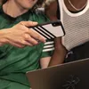 Two people are looking at a phone with an Adidas case and a laptop. Anteprima dell’immagine prodotto