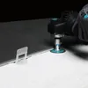 A hand wearing a glove is using a power tool to cut a tile. A tile leveling spacer is visible. Anteprima dell’immagine prodotto