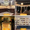 A collage of four images showing LED strip lights used in different home settings: a kitchen, a wardrobe, a desk area, and a bookshelf. Each image has a text overlay indicating the location. Produktbild-Vorschau