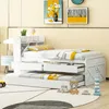 A white wooden bed with a pull-out trundle bed and drawers, set up in a child's room with artwork on the wall and toys on the floor. Podgląd zdjęcia produktu