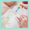 A close-up of a baby's diaper with a hand demonstrating how to adjust a tab. Podgląd zdjęcia produktu