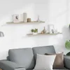 Two white and oak-effect wall shelves are mounted on a white wall above a gray sofa with cushions. Náhled obrázku produktu
