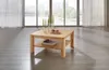 A wooden coffee table is placed in a bright room with large windows overlooking a body of water and buildings. Produktbild-Vorschau
