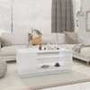 A white coffee table is placed in a living room setting with a sofa in the background. Náhľad obrázku produktu