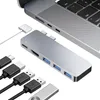 A silver USB-C hub is shown connected to a silver laptop, with various cables and a USB drive nearby. Produktbild-Vorschau