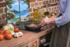 A person cooking in a kitchen with a decorative panel in the background. Produktbild-Vorschau