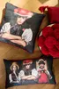 Two pillows with artistic prints of people in traditional clothing, placed on a wooden floor. A bowl of red pom-poms is also visible. Produktbild-Vorschau