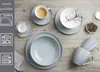 A collection of grey-blue porcelain tableware, including plates, bowls, and cups, arranged on a wooden surface. Produktbild-Vorschau