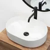 A white oval basin sink with a black faucet is placed on a wooden countertop. A round mirror is visible in the background. Anteprima dell’immagine prodotto