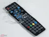 A black remote control with many buttons is shown on a white surface, with water splashing around it. Produktbild-Vorschau