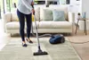 A person is vacuuming a rug in a living room. Produktbild-Vorschau
