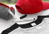 A red cap, a gray pencil case, two t-shirts, a laundry marker, and a pen are arranged on a wooden surface. Produktbild-Vorschau