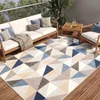 An outdoor patio scene with a sofa, chairs, a coffee table, and a geometric patterned rug.