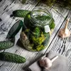 A jar of pickles with cucumbers, dill, and garlic on a wooden table. Podgląd zdjęcia produktu