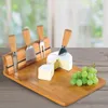 A cheese board set with cheese, grapes, and knives on a wooden table. Produktbild-Vorschau