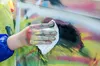 A hand covered in paint is wiping a surface with a white cloth. The surface is covered in colorful spray paint. Produktbild-Vorschau