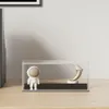A display case with an astronaut figurine and a crescent moon sculpture on a wooden surface. Produktbild-Vorschau