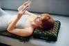 A woman is lying on a couch with an acupressure mat and pillow under her back and head, while looking at her phone. Náhľad obrázku produktu