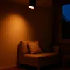 A dark room with a spotlight illuminating a beige sofa and a window showing the night sky. Náhľad obrázku produktu