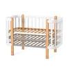 A baby crib with wooden legs and white bars, shown on a white background. Produktbild-Vorschau