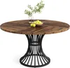 A round wooden dining table with a black metal base, decorated with a vase of greenery and a bowl of apples. Podgląd zdjęcia produktu