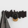 A dark brown coat rack with 5 movable hooks is mounted on a white wall. A gray coat is hanging on the leftmost hook, and a black and tan baseball cap is hanging on the middle hook. Náhľad obrázku produktu