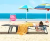 A woman is lying on a beach lounger on a sandy beach with the ocean and sky in the background. There are two beach umbrellas providing shade. Náhled obrázku produktu