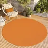 An orange circular rug on a wooden deck with a chair and plants. Voir les images du produit