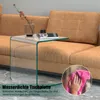 A clear glass side table is placed next to a brown sofa in a living room setting. A vase with decorative branches sits on the table. Produktbild-Vorschau