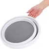 A hand is shown holding the edge of a white rotating organizer with a gray textured surface. Produktbild-Vorschau