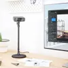 A webcam on a stand is placed on a desk next to a large monitor displaying software. Produktbild-Vorschau