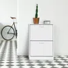 A white shoe cabinet with two drawers stands against a white wall, next to a bicycle. The floor has a black and white checkered pattern. Voir les images du produit
