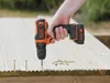 A hand holding a Black & Decker cordless drill, screwing a screw into a wooden deck. Podgląd zdjęcia produktu