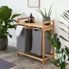 A bamboo laundry rack with two gray laundry bags, placed next to a large potted plant in a room with a white wall and gray floor. Produktbild-Vorschau