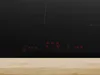 A close-up shot of a black induction cooktop with red digital displays and markings. Anteprima dell’immagine prodotto