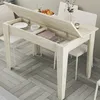 A dining table with its top open, revealing storage compartments. Plates, bowls, and folded fabric are visible inside. The table is set in a dining area with chairs and a floor with a herringbone pattern. Anteprima dell’immagine prodotto