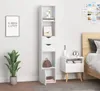 A tall, narrow white bookshelf with drawers and a door, placed in a bedroom setting next to a nightstand and bed. Produktbild-Vorschau