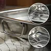 Close-up of a stainless steel roasting pan with a rack inside, resting on a checkered cloth. Voir les images du produit