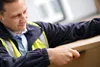 A man in a safety vest is opening a cardboard box with a utility knife. Produktbild-Vorschau