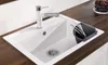 A white kitchen sink with a white faucet and a gray utensil holder with utensils inside. The sink is set into a dark wood countertop. Produktbild-Vorschau