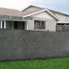 A grey privacy screen fence is in the foreground, with a house and another building in the background. Produktbild-Vorschau