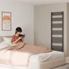 A woman is reading a book in bed, with a towel radiator in the background. Produktbild-Vorschau