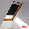 A black roller blind is partially covering a wooden framed skylight window, with sunlight casting shadows on the white walls. Produktbild-Vorschau
