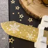 A close-up of a Christmas cracker with a gold and white snowflake pattern, surrounded by gold star confetti and a wooden slice. Produktbild-Vorschau