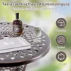 A close-up of a round outdoor table with a bottle of alcohol, a glass, and a book on it. Icons and text describing product features are on the right. Náhled obrázku produktu