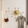 A gold coat rack mounted on a white wall, holding a straw hat, a brown purse, and a patterned dress on a hanger. Voir les images du produit