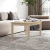 A coffee table with books and a blanket on it, placed in a living room setting with a sofa and a plant. Produktbild-Vorschau