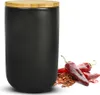 A black ceramic storage jar with a wooden lid, next to red chili peppers and chili flakes. Produktbild-Vorschau